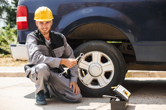 young smiling mechanic work clothes yellow hardhat happily looking camera holding wrench changing car wheel outdoor 1